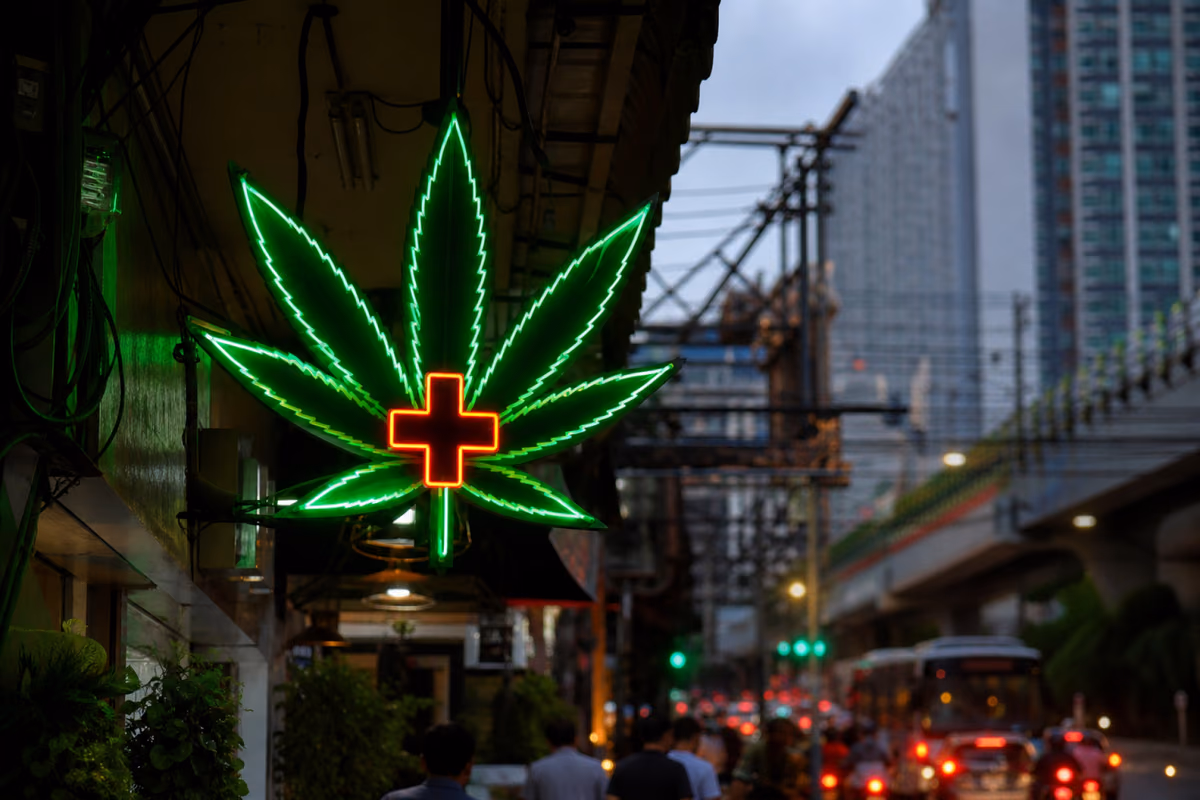 Insegna al neon a forma di foglia di cannabis con croce medica su una strada trafficata di Bangkok al crepuscolo